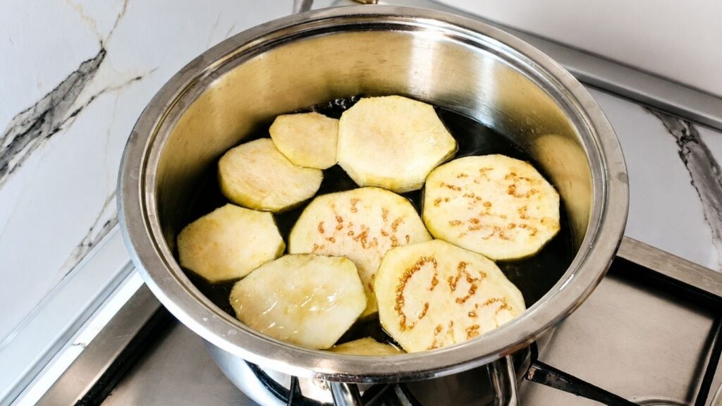 Blanching eggplant slices in salted boiling water before breading and frying.