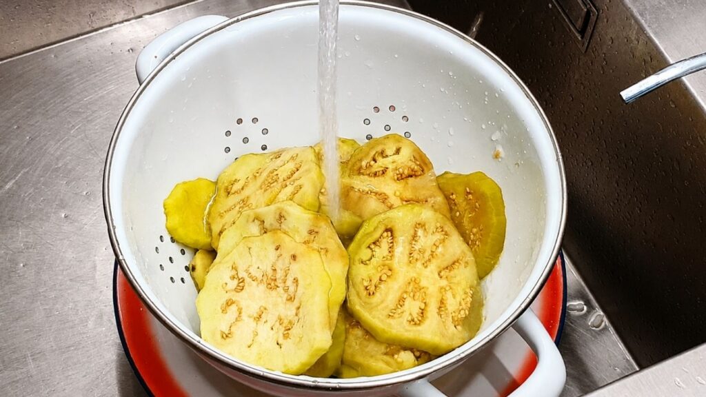 Rinsing blanched eggplant slices under cold water to stop the cooking process.