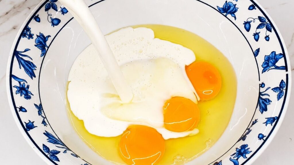 Pouring eggs and milk into a bowl to prepare the breading mixture for eggplant.