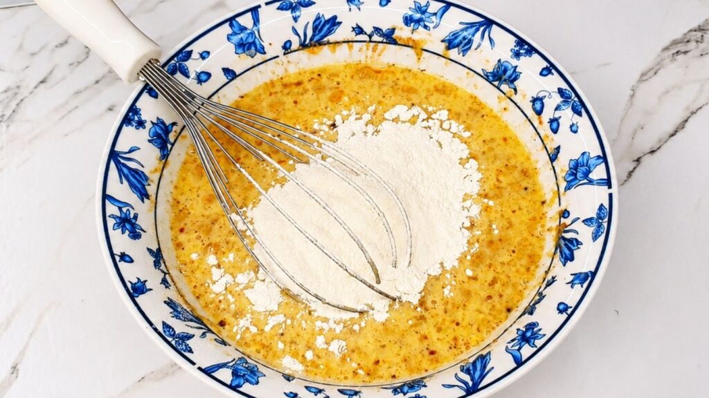 Adding seasonings and flour to the egg and milk mixture for breaded eggplant.