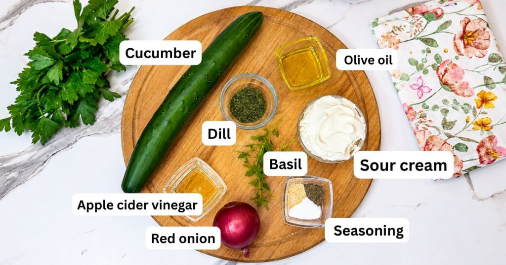 Ingredients for creamy cucumber salad, including English cucumber, red onion, sour cream, apple cider vinegar, olive oil, dill, garlic powder, basil, salt, and black pepper.