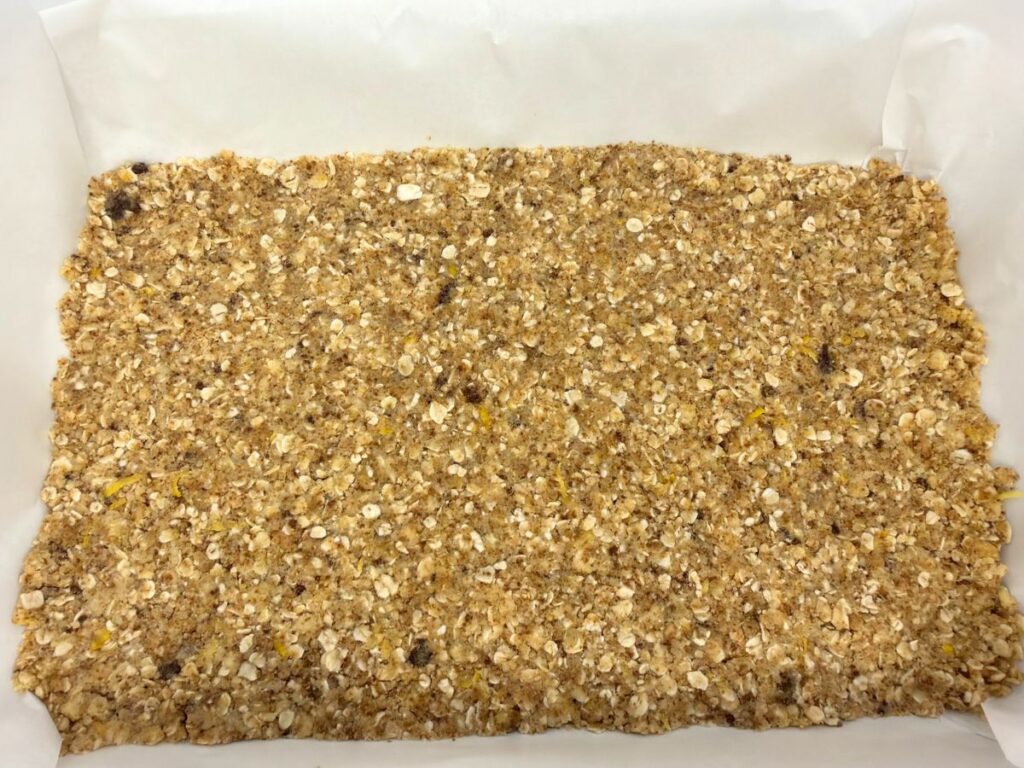 Pressed oat crust in a parchment-lined baking pan for cherry crumb bars.