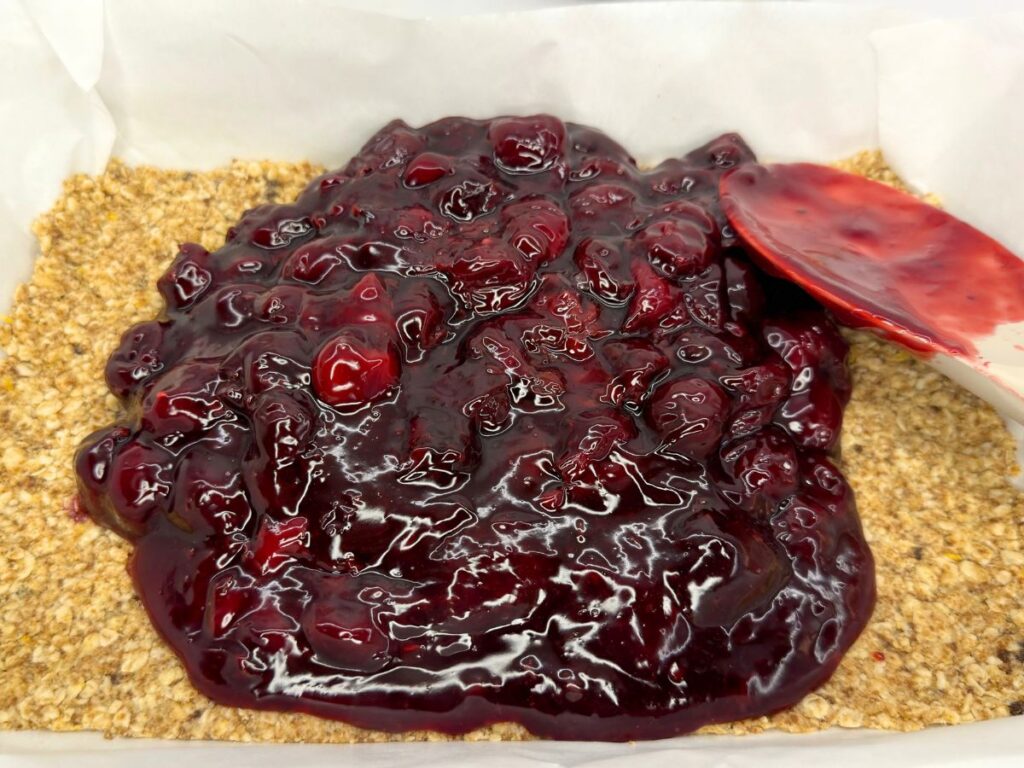 Thick cherry filling spread over the baked crust in a parchment-lined pan.