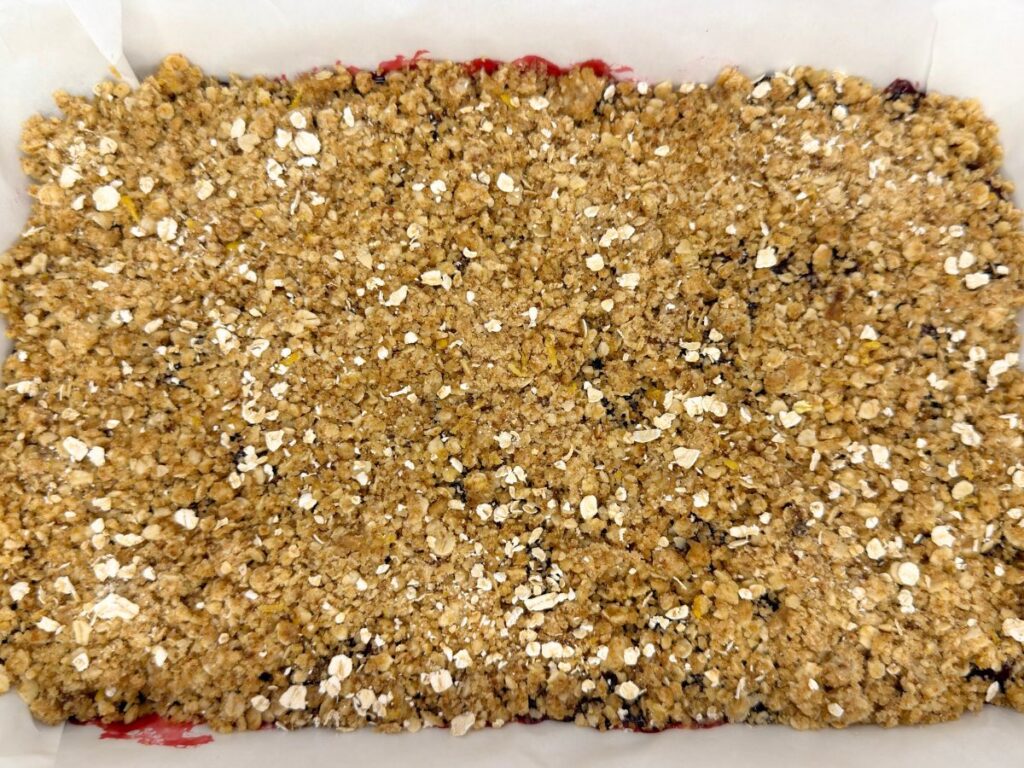 Reserved oat crumble topping sprinkled over the cherry filling in the baking pan.