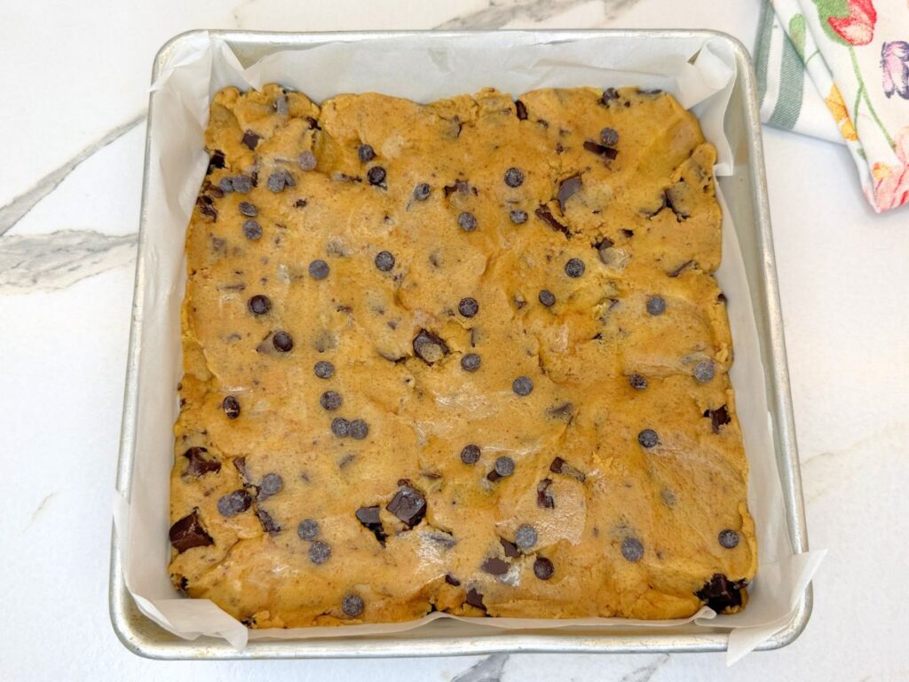 Chocolate chip cookie bar dough spread in a baking pan and ready to bake.