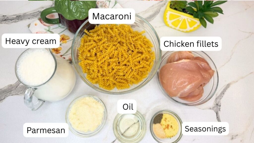 Ingredients for creamy chicken pasta arranged on a table, including chicken breasts, pasta, cooking cream, Parmesan cheese, oil, water, and seasonings.