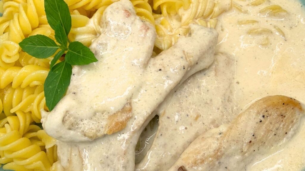 Close-up of tender chicken fillets in a creamy white sauce served with rotini pasta.