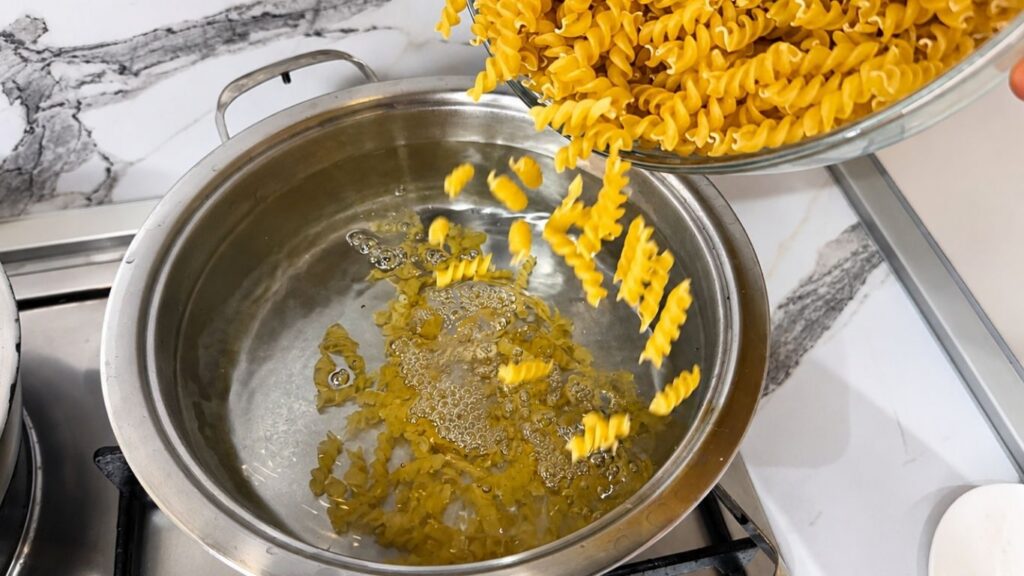 Pouring pasta into a pot of boiling salted water for creamy chicken pasta.