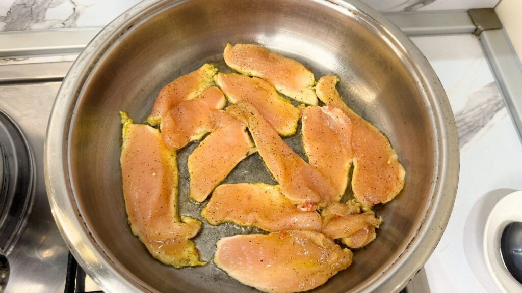 Cooking thinly sliced chicken in a skillet for creamy chicken pasta.