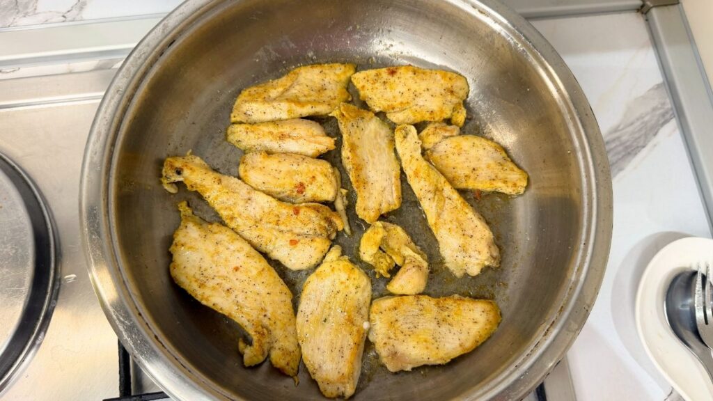 Cooking thinly sliced chicken in a skillet for creamy chicken pasta.