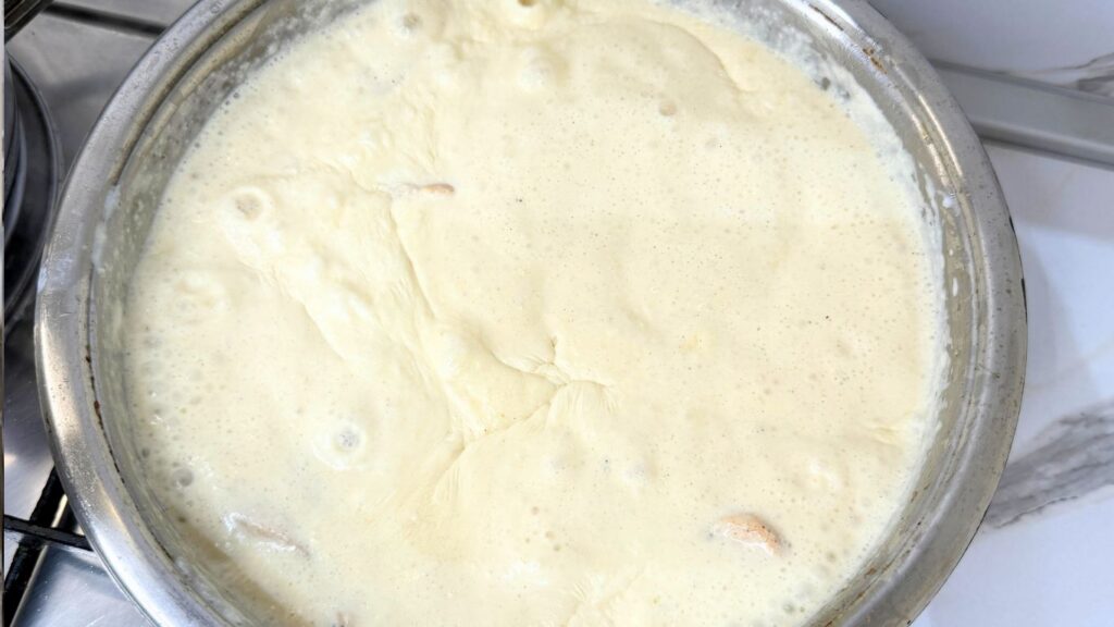 Adding cooking cream, Parmesan cheese, and water to the cooked chicken in a skillet.