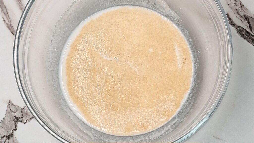 Activated yeast mixture sitting in a large bowl, showing a frothy, foamy, and bubbly texture.