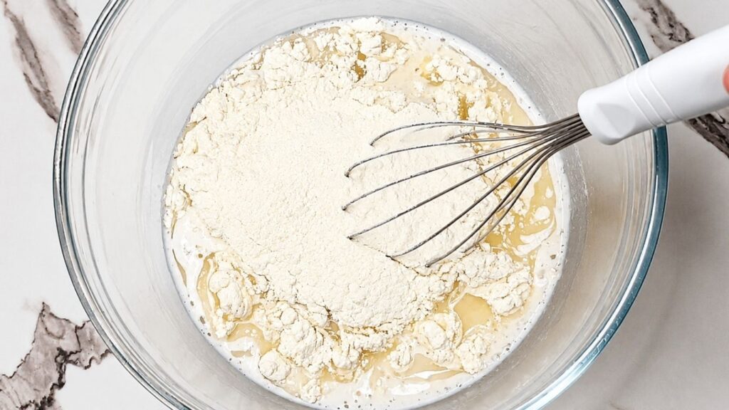 Adding oil, salt, and flour to the activated, foamy yeast mixture in a large mixing bowl.