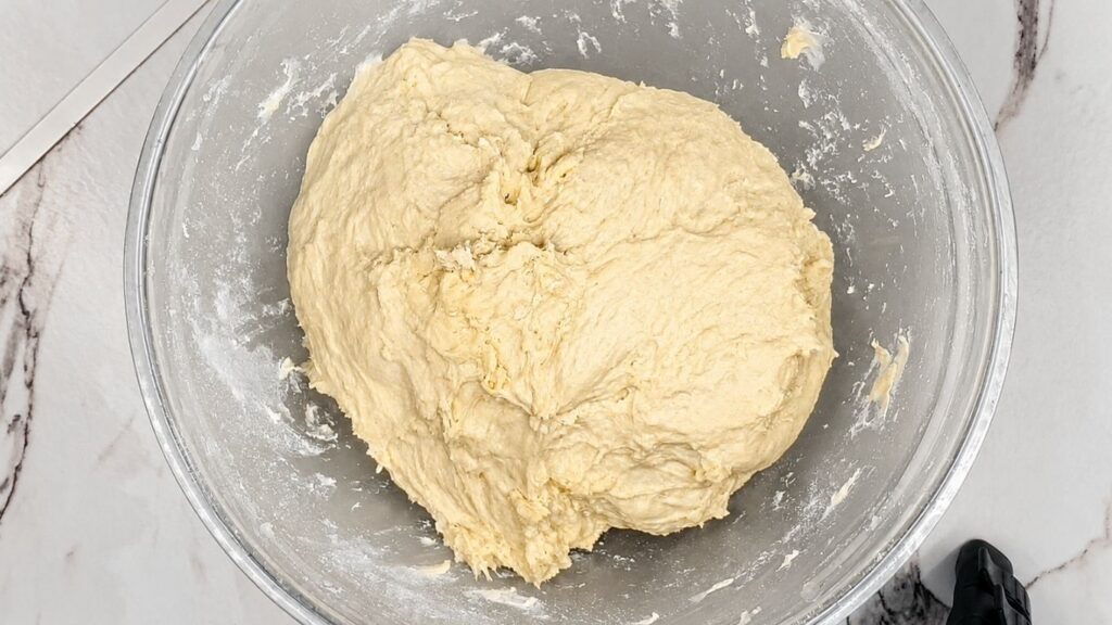 Smooth, freshly kneaded crescent roll dough shaped into a ball inside a large mixing bowl, ready to rise.