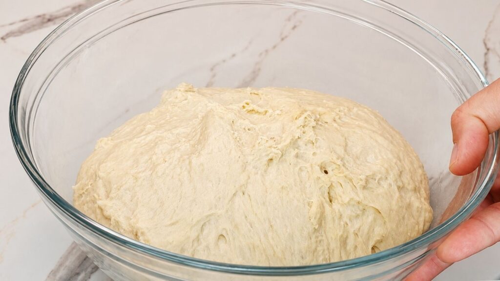 Soft crescent roll dough doubled in size and fully risen in a large mixing bowl.