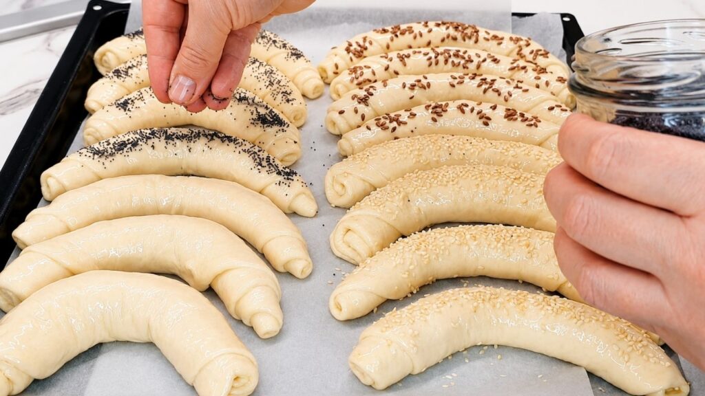 Sprinkling seeds on top of shaped, raw crescent rolls on a baking sheet right before baking.