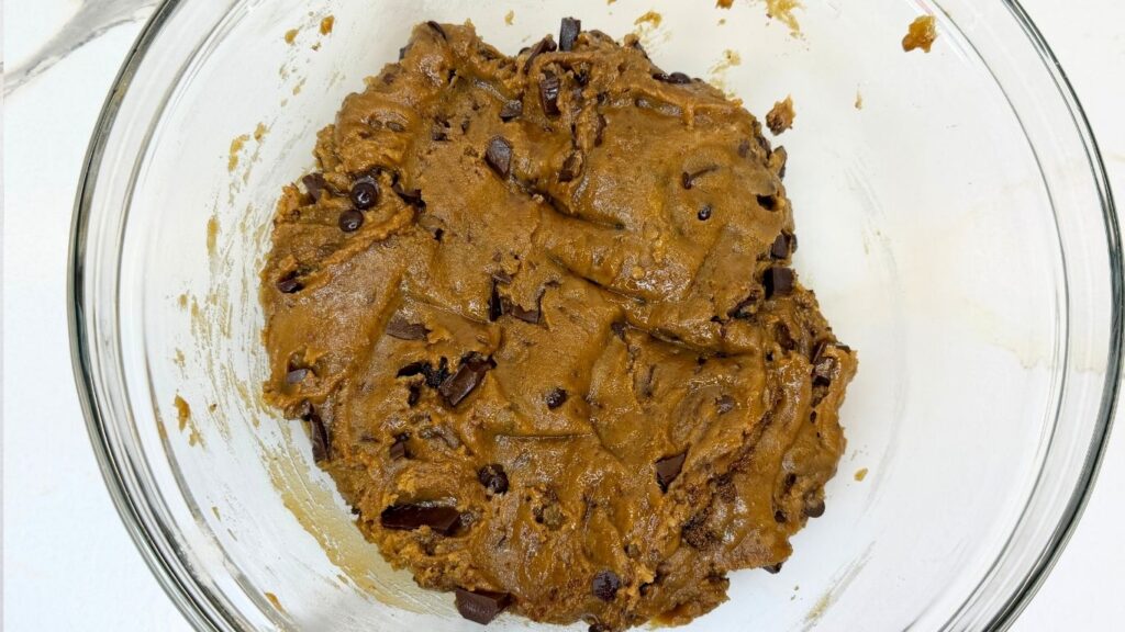 A mixing bowl filled with freshly mixed chocolate chip cookie dough, loaded with chocolate chips and chunks, ready to be covered and chilled in the refrigerator.