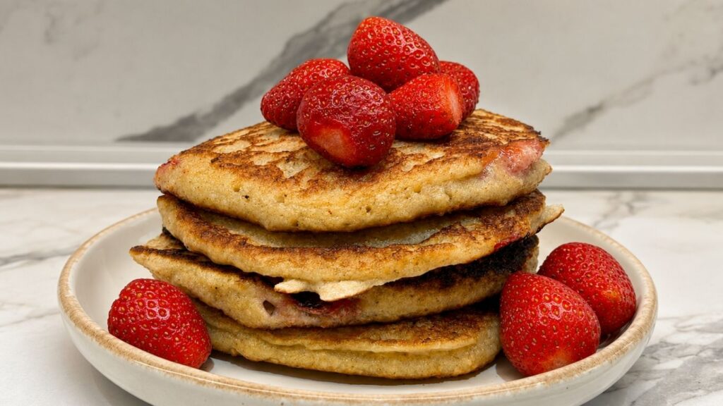 Flourless gluten-free banana pancakes with strawberries, cut open to show the soft oat texture and topped with fresh strawberries and date sauce.