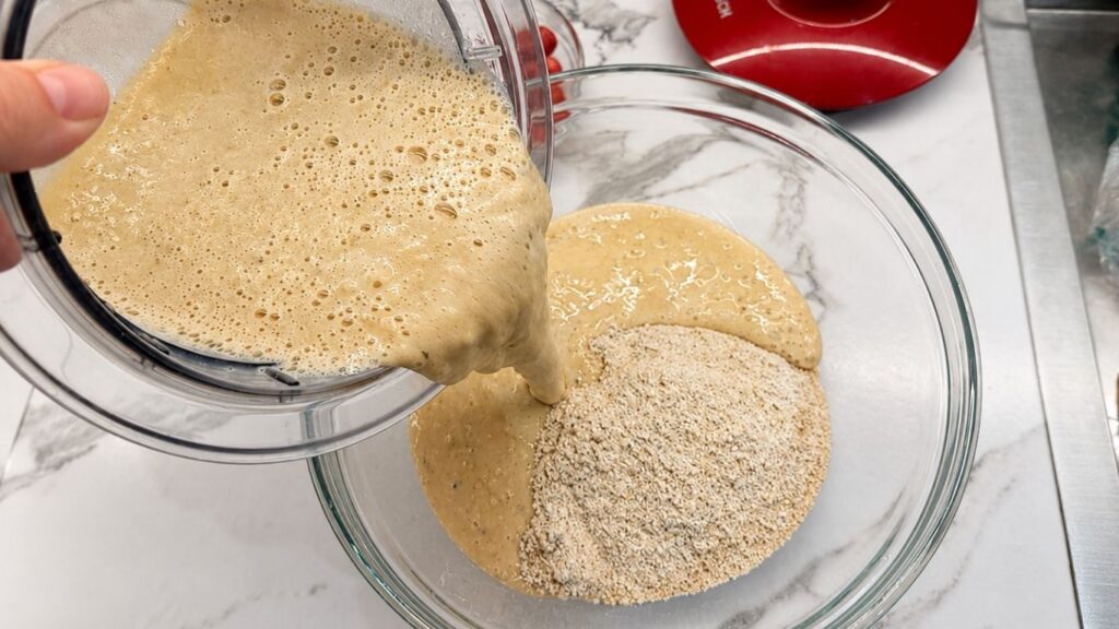 Pouring the blended wet ingredients into a bowl of ground oats to make gluten-free banana pancake batter.