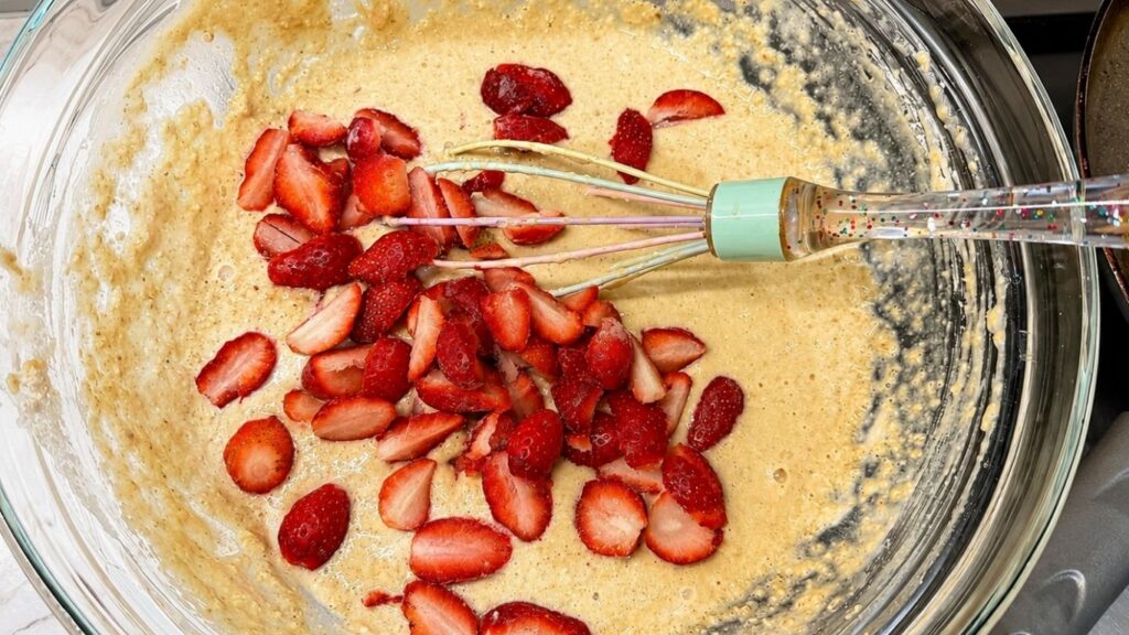 Adding quartered strawberries to the mixed batter for gluten-free banana pancakes