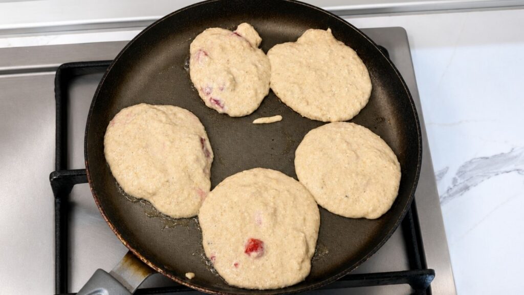 Gluten-free banana pancakes cooking in a pan until golden brown.