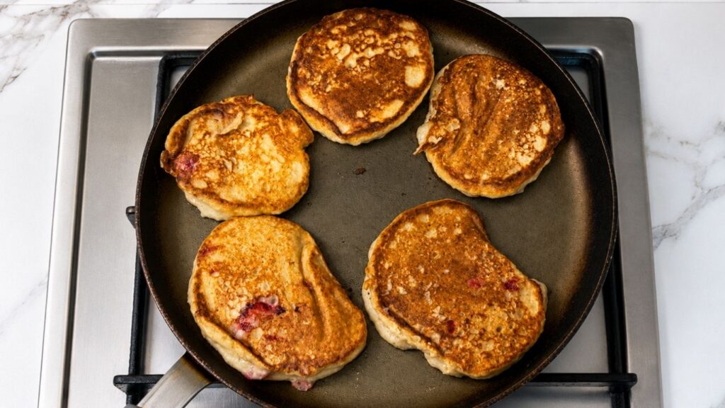 Gluten-free banana pancakes flipped in the pan and cooking until golden brown on the other side.