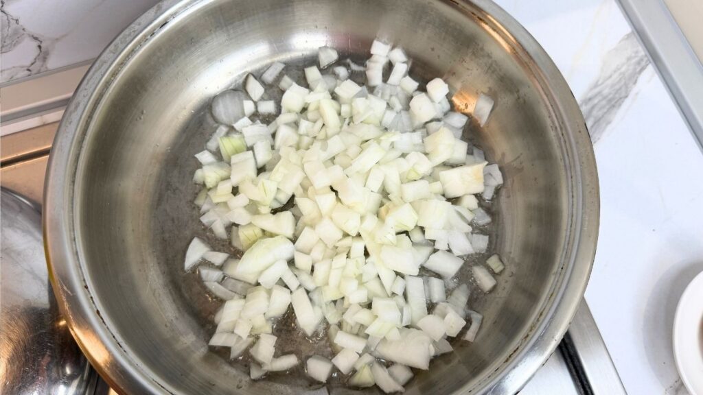 Chopped onions being sautéed in a deep skillet for a one-pot chicken and rice recipe.