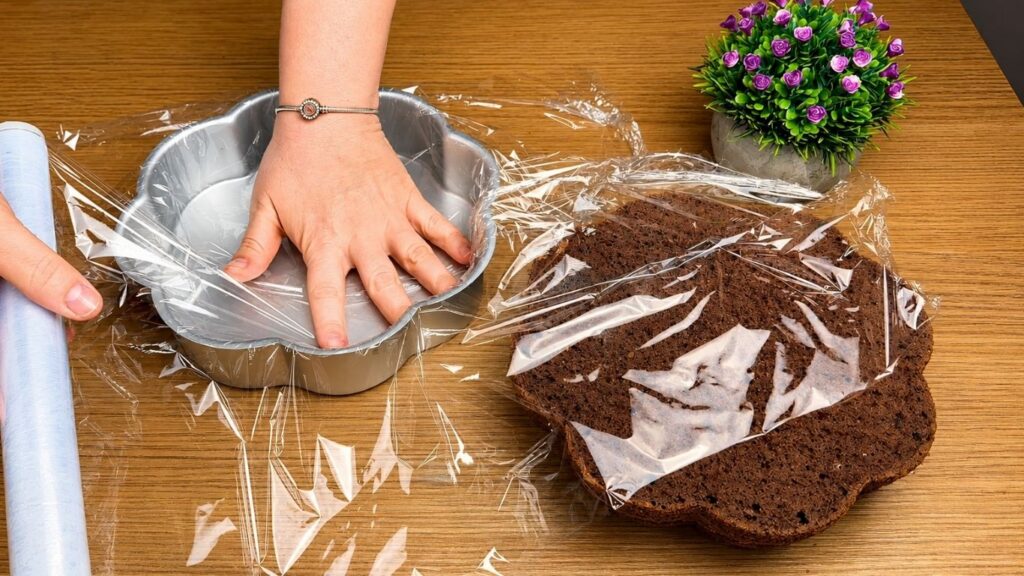 Lining the cake pan with plastic wrap.