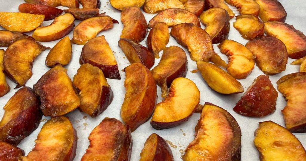 Sliced peaches arranged on parchment paper on a baking sheet, ready to bake for Peach Cobbler Cheesecake.