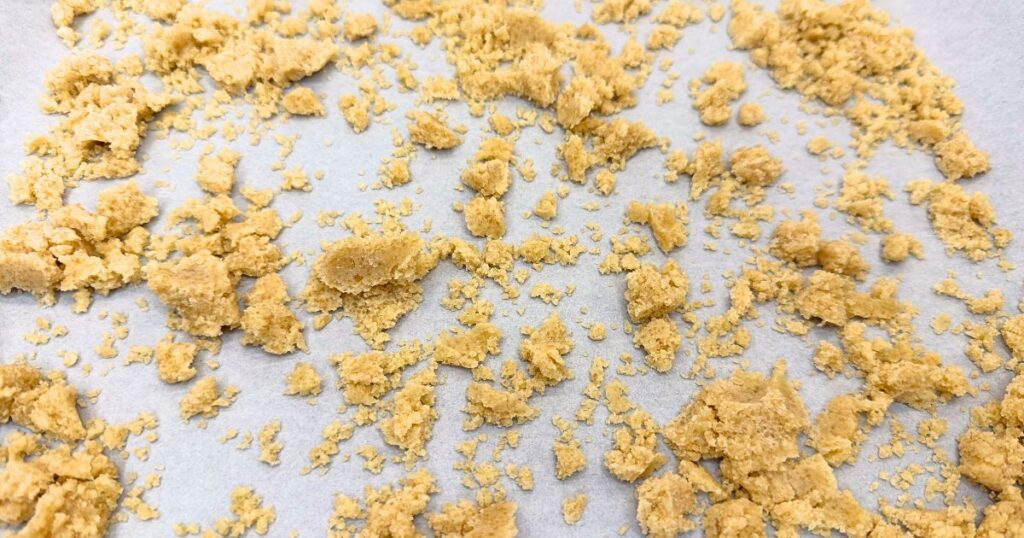 Crumble topping spread on parchment paper on a baking sheet, ready to bake for Peach Cobbler Cheesecake.