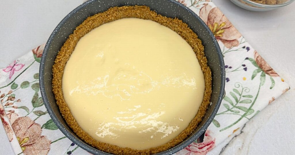 Half of the cheesecake filling spread over the graham cracker crust in a springform pan.