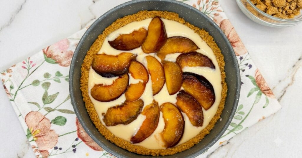 Baked peach slices arranged over the first layer of cheesecake filling in a springform pan.