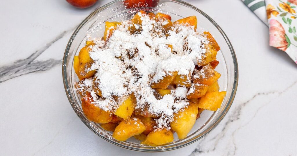 Peaches mixed with sugar, cornstarch, lemon juice, vanilla, cinnamon, and salt in a bowl for Peach Cobbler.