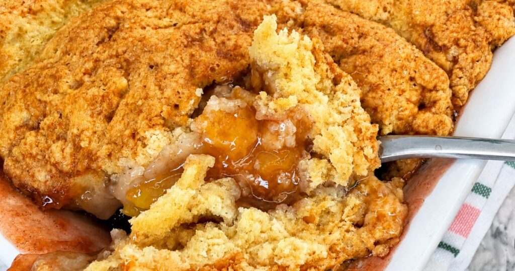 Freshly baked Peach Cobbler with a golden topping and bubbling peach filling in a baking dish.