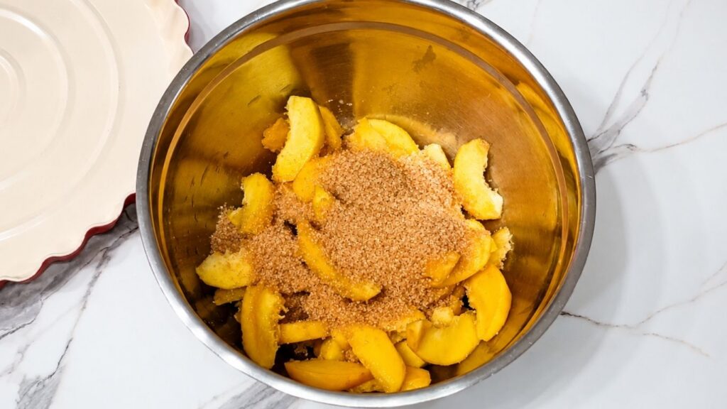Fresh sliced peaches mixed with brown sugar in a bowl for homemade peach upside down cake