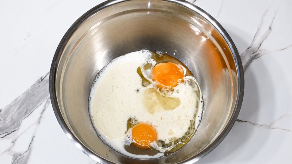 Eggs, milk, oil, and brown sugar in a bowl for making peach upside down cake batter