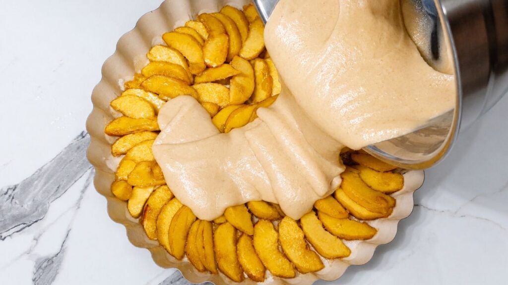 Pouring soft cake batter over peach slices in a round baking pan for homemade peach upside down cake
