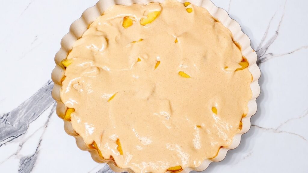 Pouring soft cake batter over peach slices in a round baking pan for homemade peach upside down cake