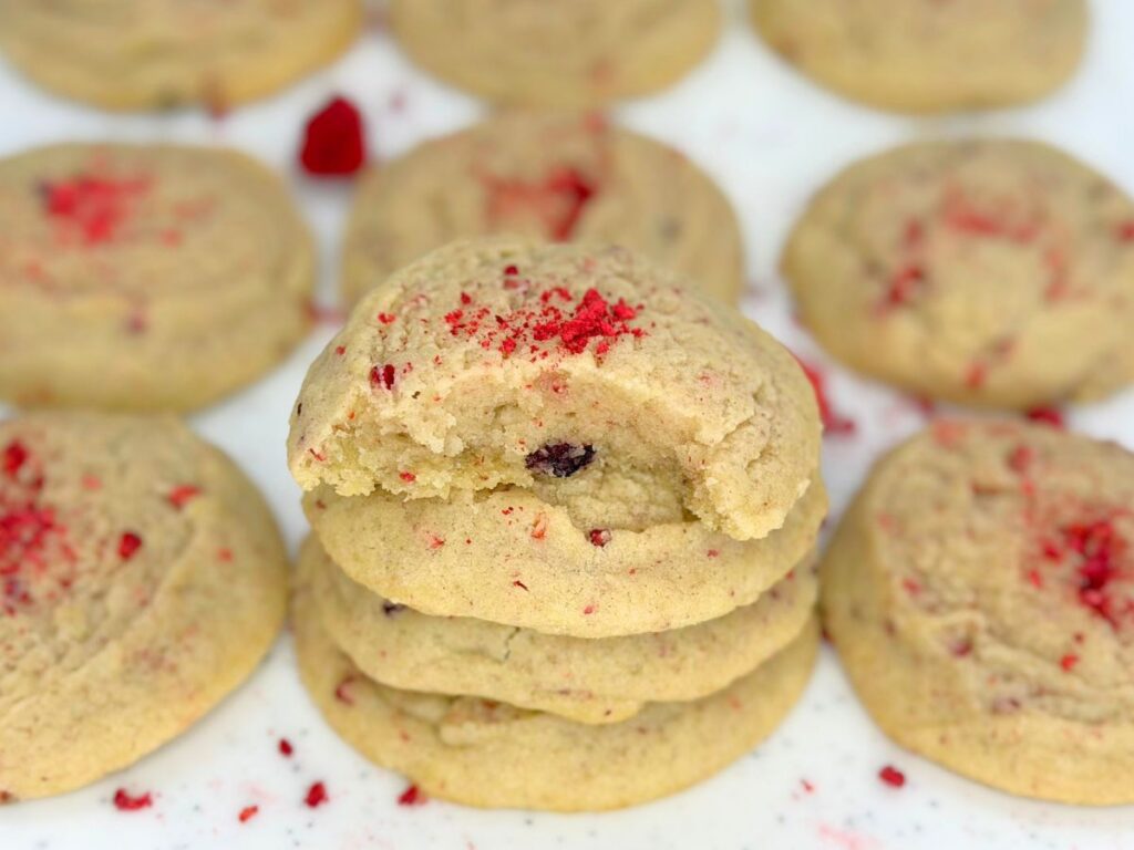 Stack of soft and chewy raspberry sugar cookies topped with crushed dried raspberries and surrounded by more cookies.