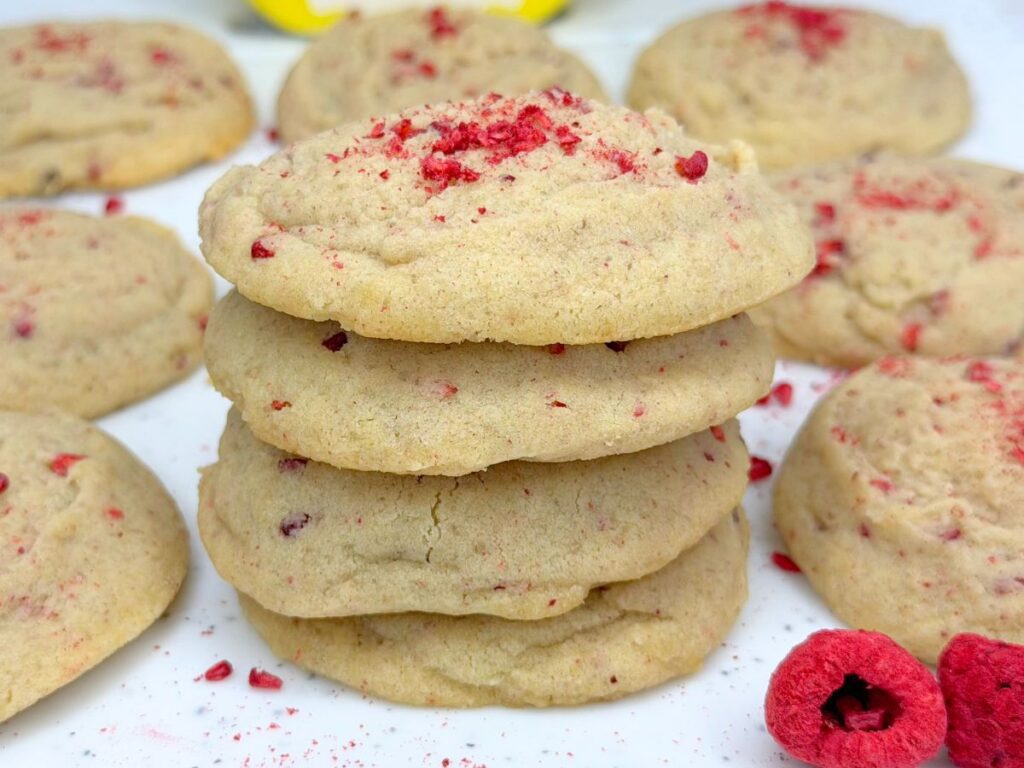 Stack of soft and chewy raspberry sugar cookies topped with crushed dried raspberries and surrounded by more cookies.