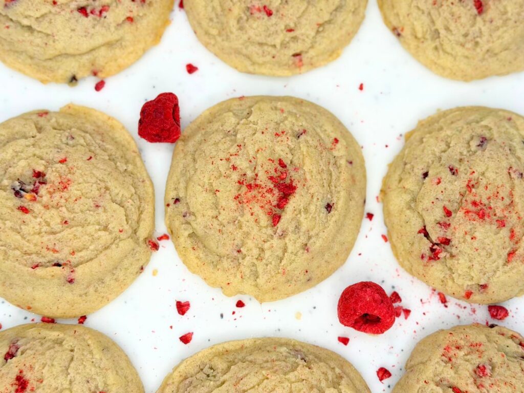 Overhead view of soft raspberry sugar cookies sprinkled with crushed dried raspberries on a white surface.