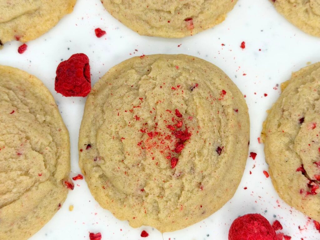 Overhead view of soft raspberry sugar cookies sprinkled with crushed dried raspberries on a white surface.