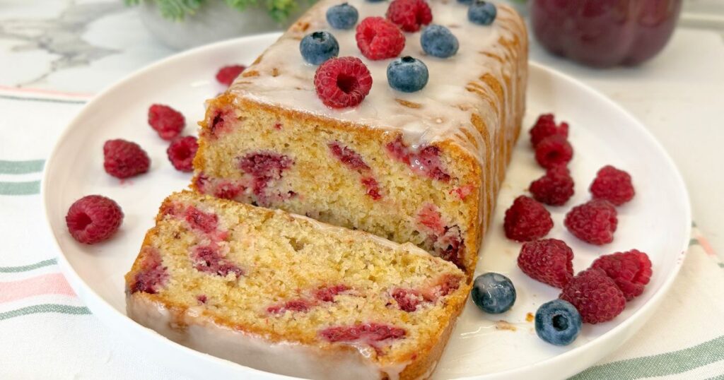 Moist raspberry bread made with fresh raspberries and topped with a sweet vanilla icing, with one slice served beside the loaf.