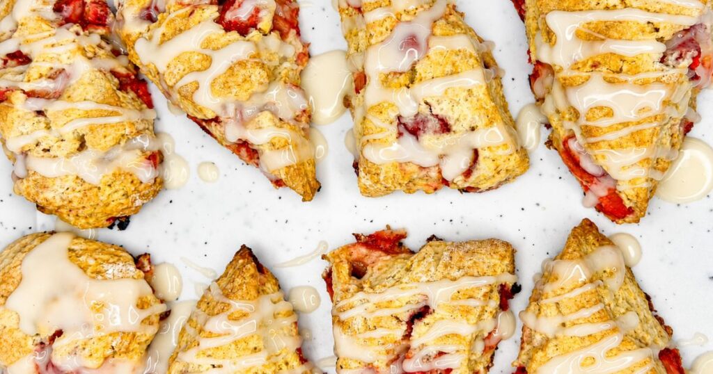 Homemade strawberry scones with frozen strawberry pieces and sweet vanilla glaze on a white serving board.