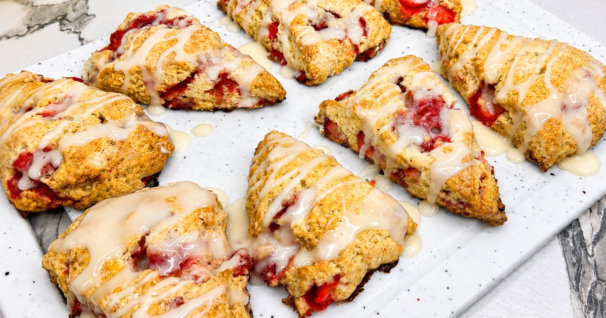 Golden strawberry scones with strawberry pieces and sweet glaze arranged on a white serving board.