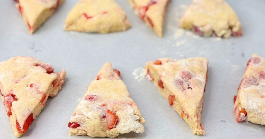 Unbaked strawberry scones arranged on parchment paper on a baking sheet.