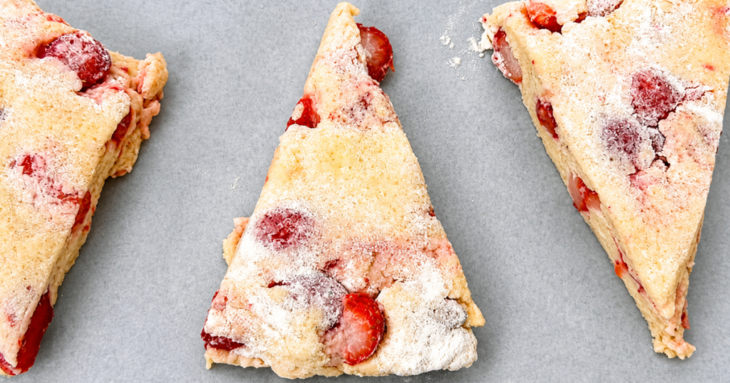 Unbaked strawberry scones arranged on parchment paper on a baking sheet.