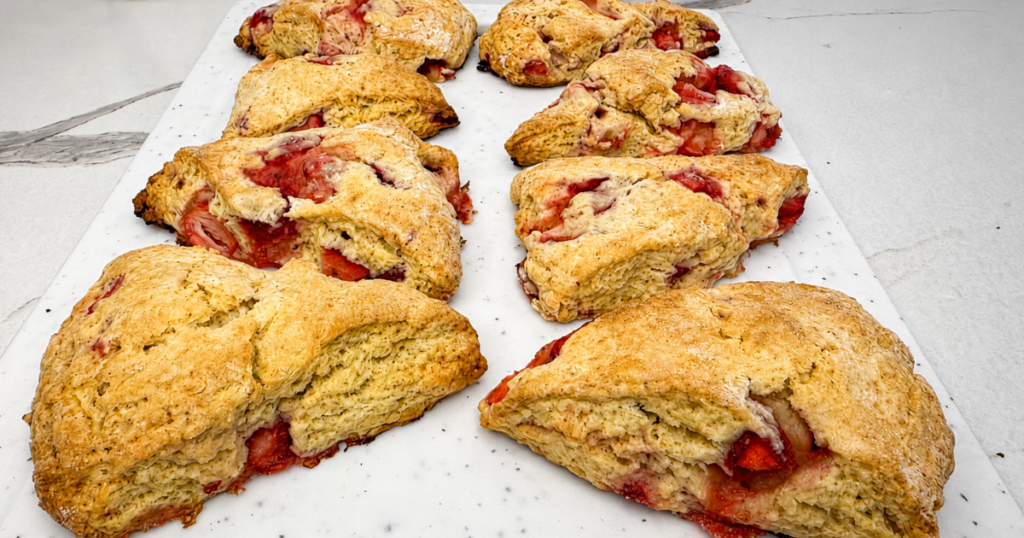 Homemade strawberry scones with frozen strawberry pieces and sweet vanilla glaze on a white serving board.