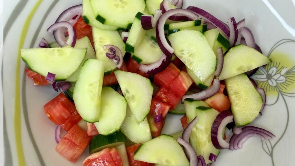Chopped cucumber, tomato, and red onion arranged in a bowl for summer cucumber salad.