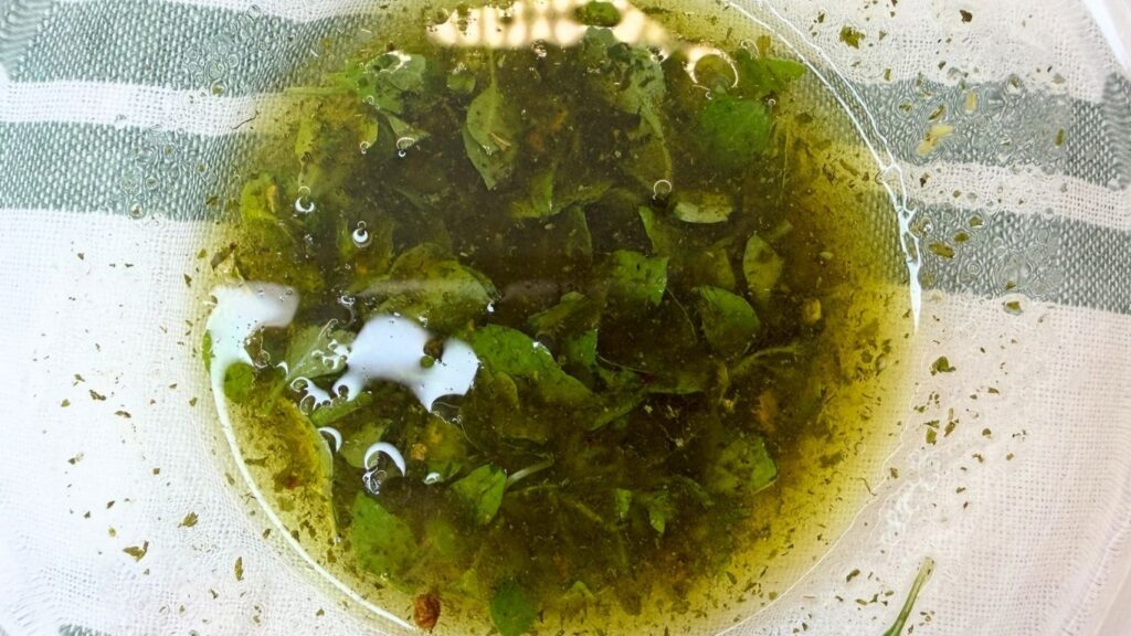 Fresh lemon, olive oil, basil, and seasonings mixed together in a bowl for cucumber salad dressing.